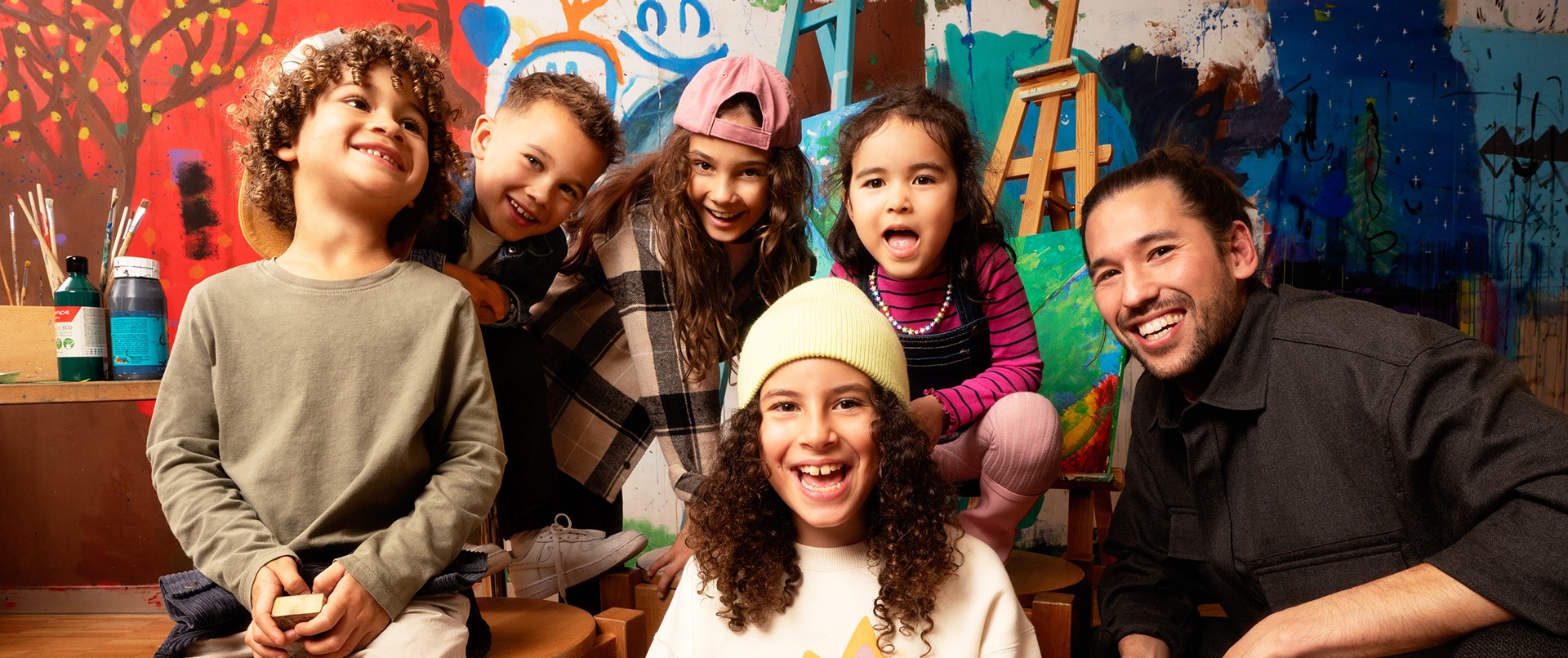 Foto mit Kindern, die l&auml;cheln und mit dem Lehrer hinter einer grossen bemalten Wand.
